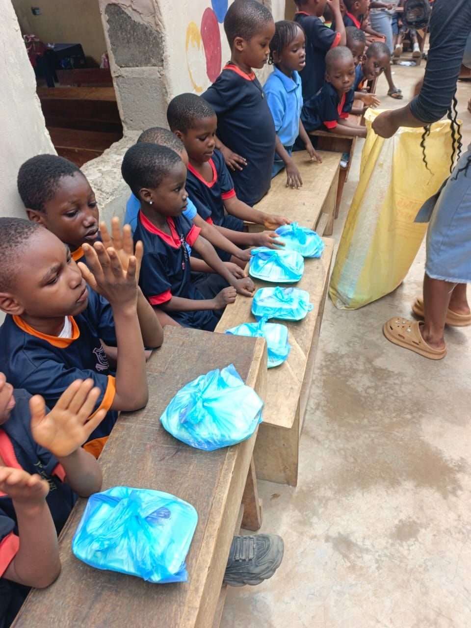 Young children being served packed lunches on wooden benches during daycare