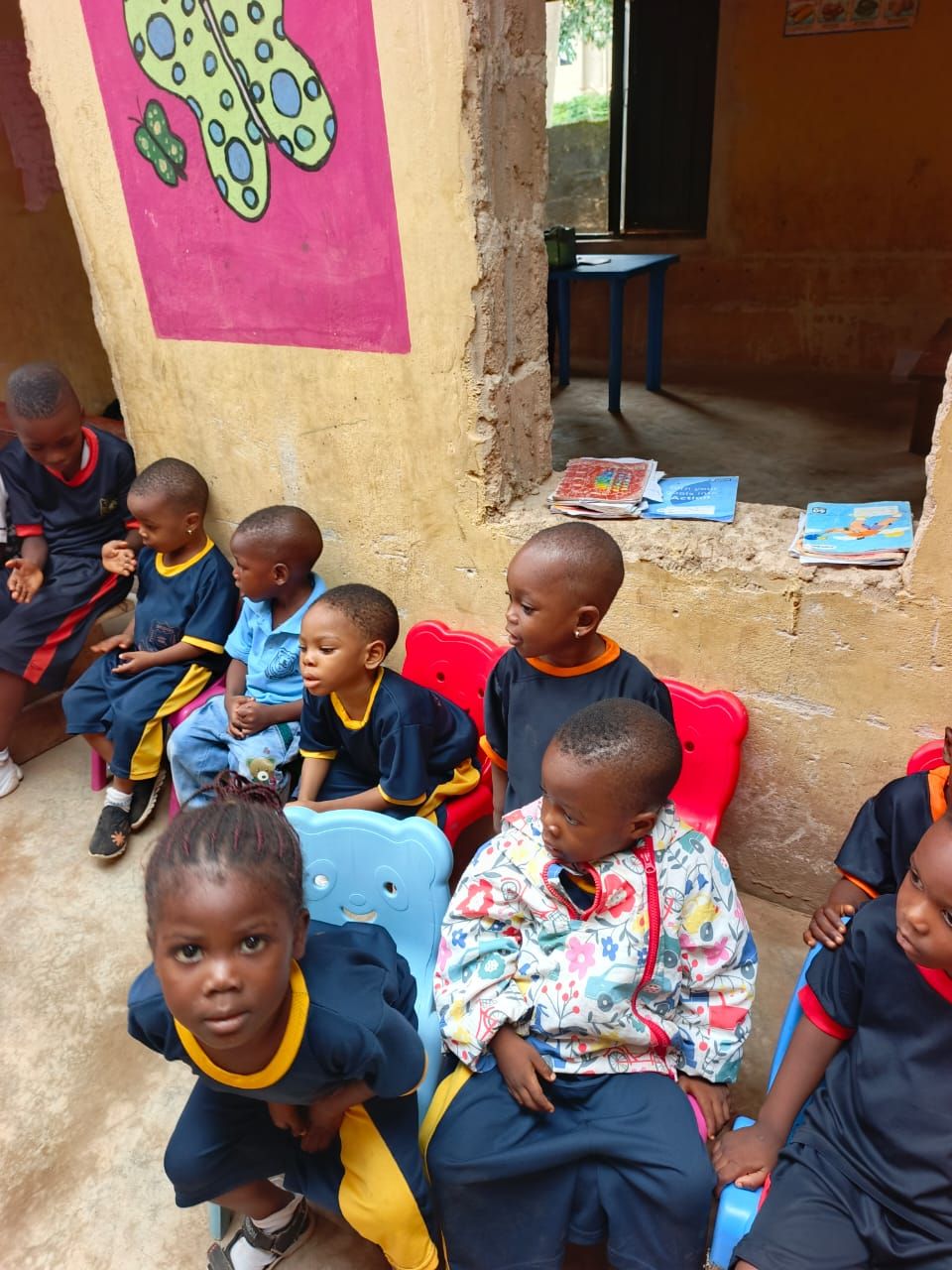 Nursery children in uniform seated on small chairs in a bright classroom