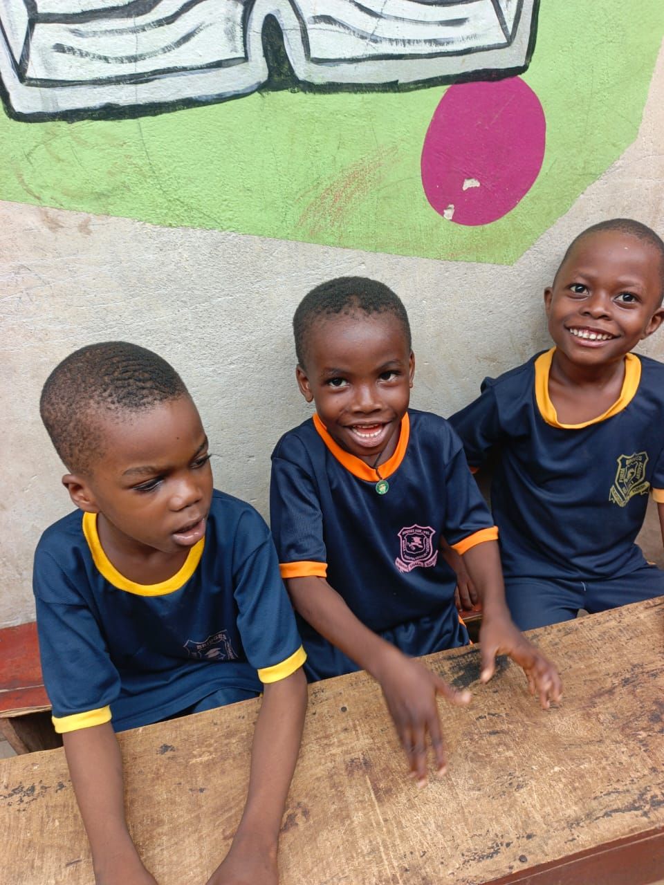 Three smiling pupils in navy and marigold sports uniform sitting together at a desk